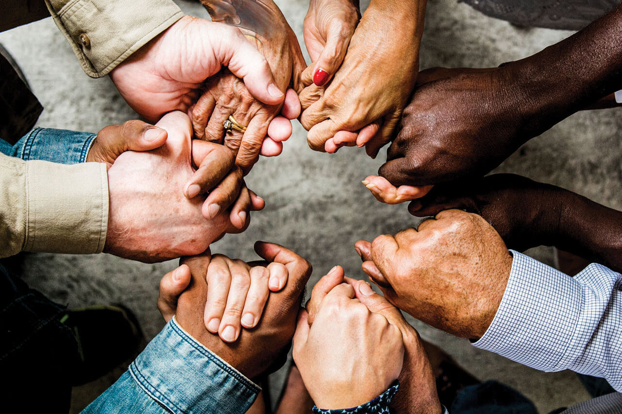 A diverse group of people stand in a circle holding hands. Image by Rawpixel, iStockphoto.com. 