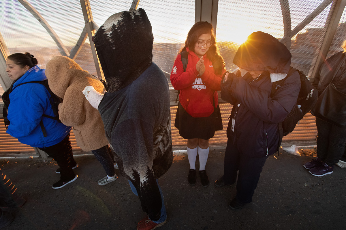 Ruth Moreno shows her brother, Lino, how to keep his hands warm as the sun rises behind them on the Santa Fe Bridge over the Rio Grande in Juárez, Mexico. They make the two-hour cross-border journey each school day to attend the United Methodist Lydia Patterson Institute in El Paso, Texas. Photo by Mike DuBose, UM News.