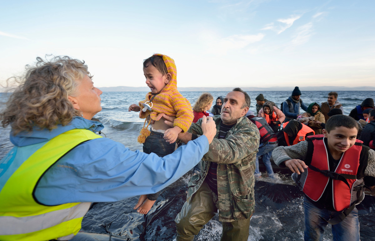 Volunteers carry a child ashore on a beach near Molyvos, on the Greek island of Lesbos, on Oct. 30, 2015, after a group of refugees crossed the Aegean Sea from Turkey in a small overcrowded boat provided by Turkish traffickers to whom the refugees paid huge sums. The refugees were received in Greece by local and international volunteers, then proceeded on their way toward western Europe. File photo by Paul Jeffrey/Life on Earth Pictures.