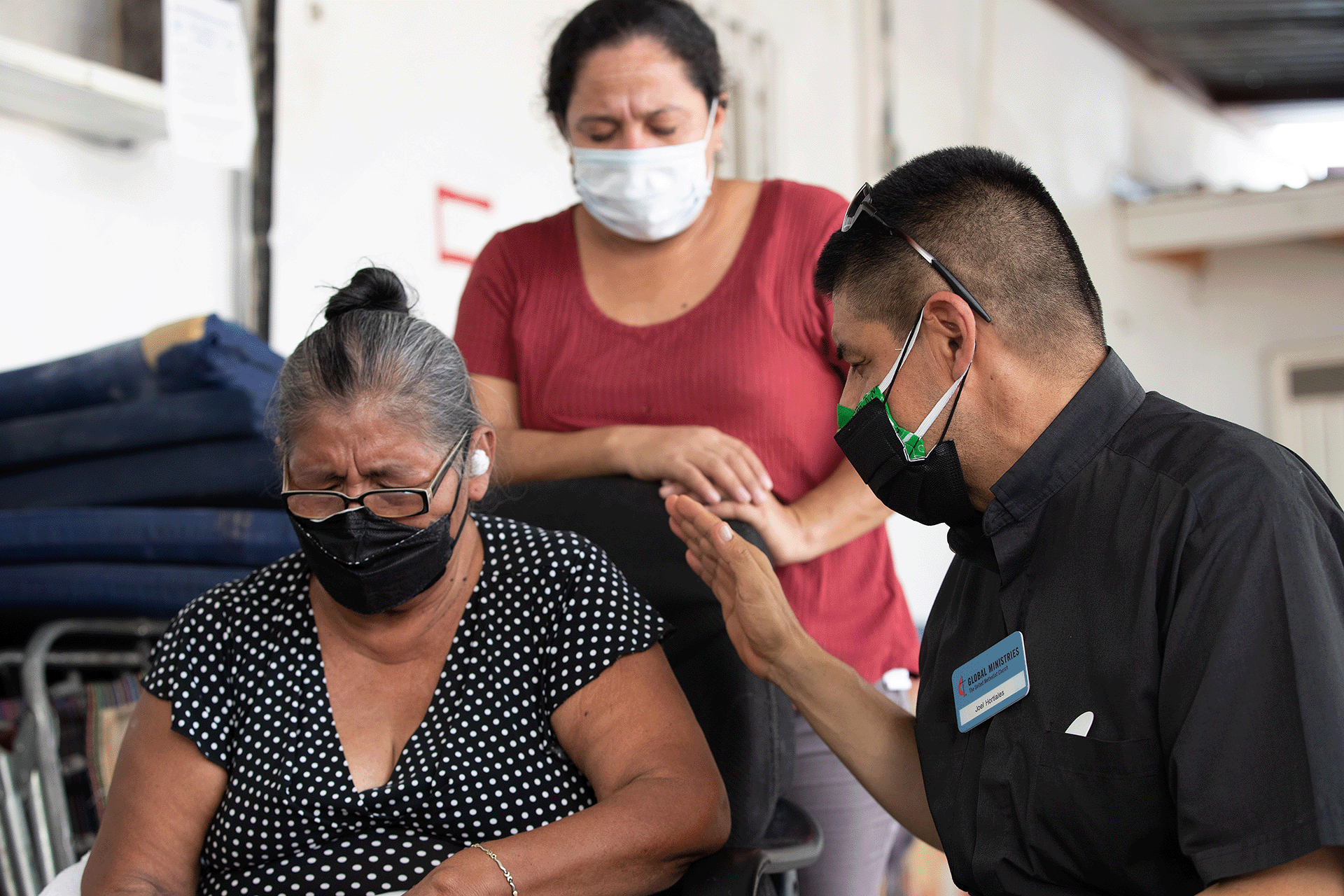 United Methodist Missionary Joel Hortiales prays with Eugenia, who fled gang violence in Guatemala, at El Camino a un Nuevo Amanecer shelter in Mexicali, Mexico. The woman behind them is also a migrant from Guatemala. Photo by Mike DuBose, UM News.