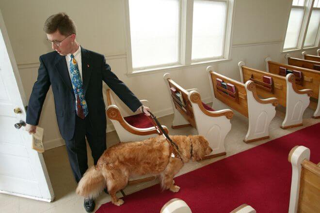The Rev. Eric Pridmore, lead by Gene, his Seeing Eye dog , brings the worship bulletins to prepare for the morning service at Goodman Memorial United Methodist Church in Cary, Miss. Photo by Mike DuBose, UMNS. 